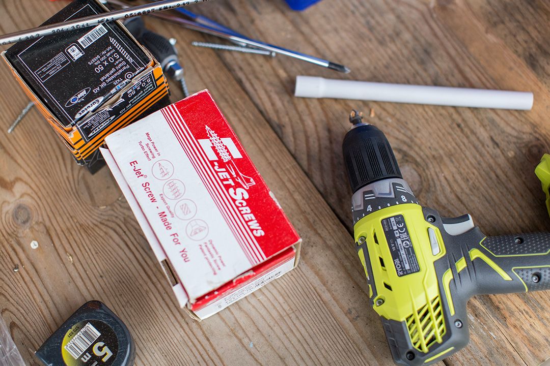 A cordless drill, fasteners, and tools laid out on a work table.