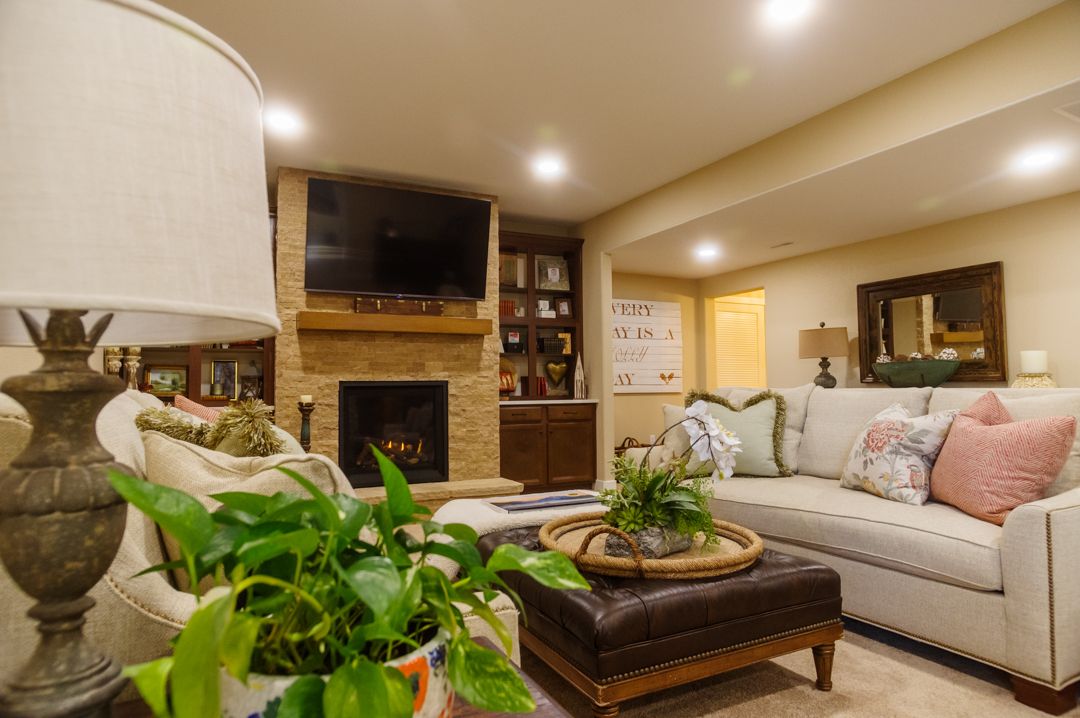 Finished basement with stone gas fireplace, mantle, mounted TV, recessed lighting, couch, coffee table, lamp, and pants.