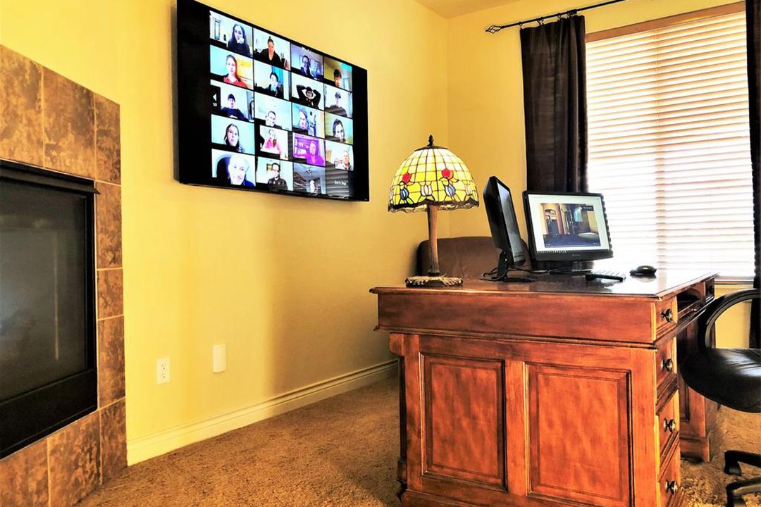 Home office with a large desk, fireplace, and tv mounted to the wall.