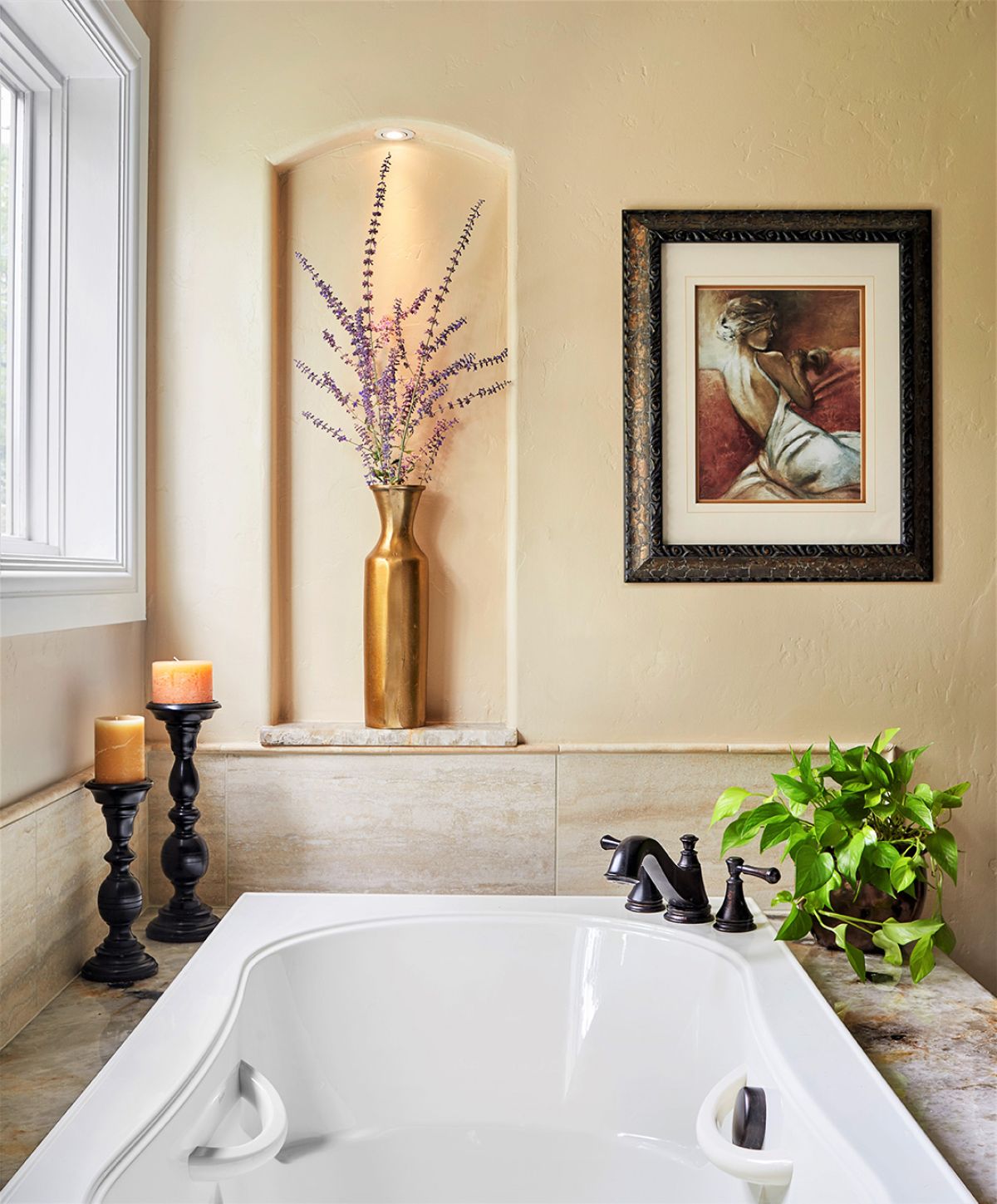 POV of luxury bath tub with candles, vase, and artwork.